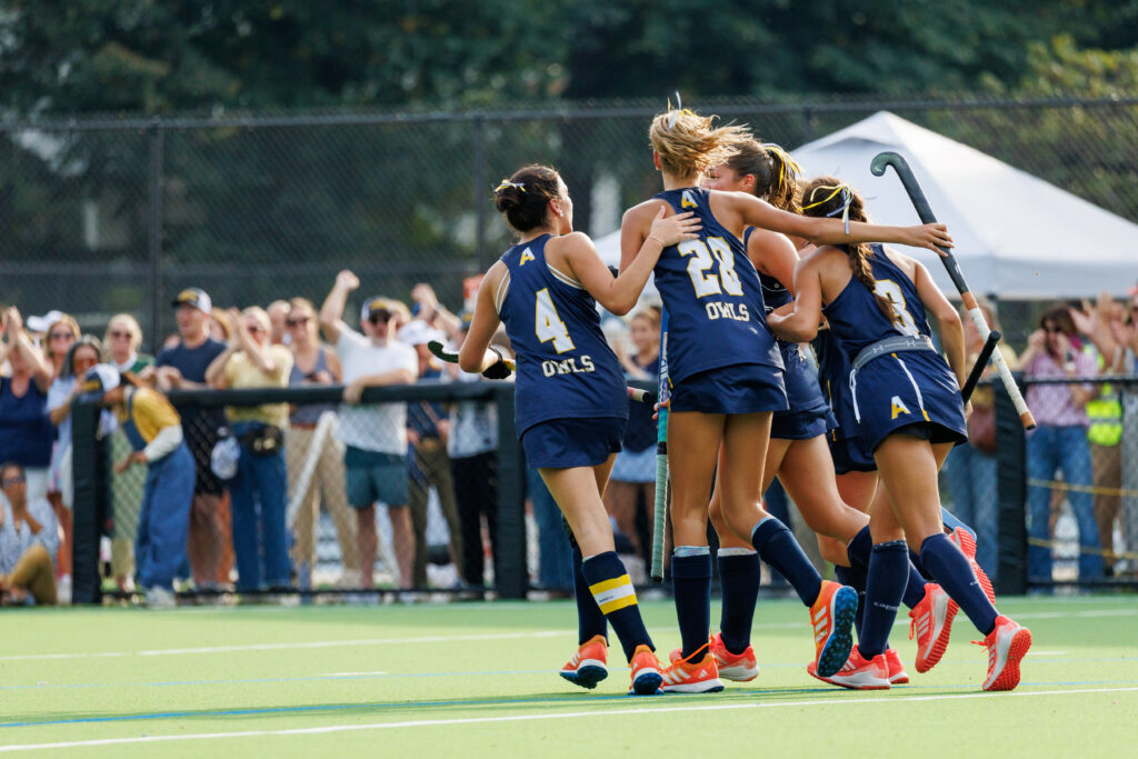 Field hockey teammates in blue uniforms celebrating together on the field
